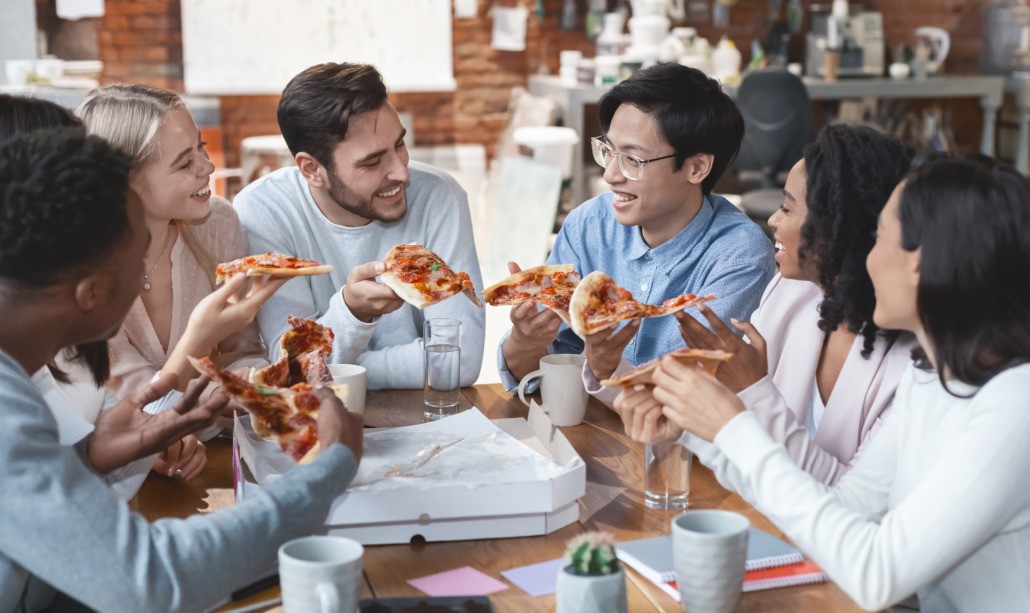 Friendly international business team enjoying pizza together in office