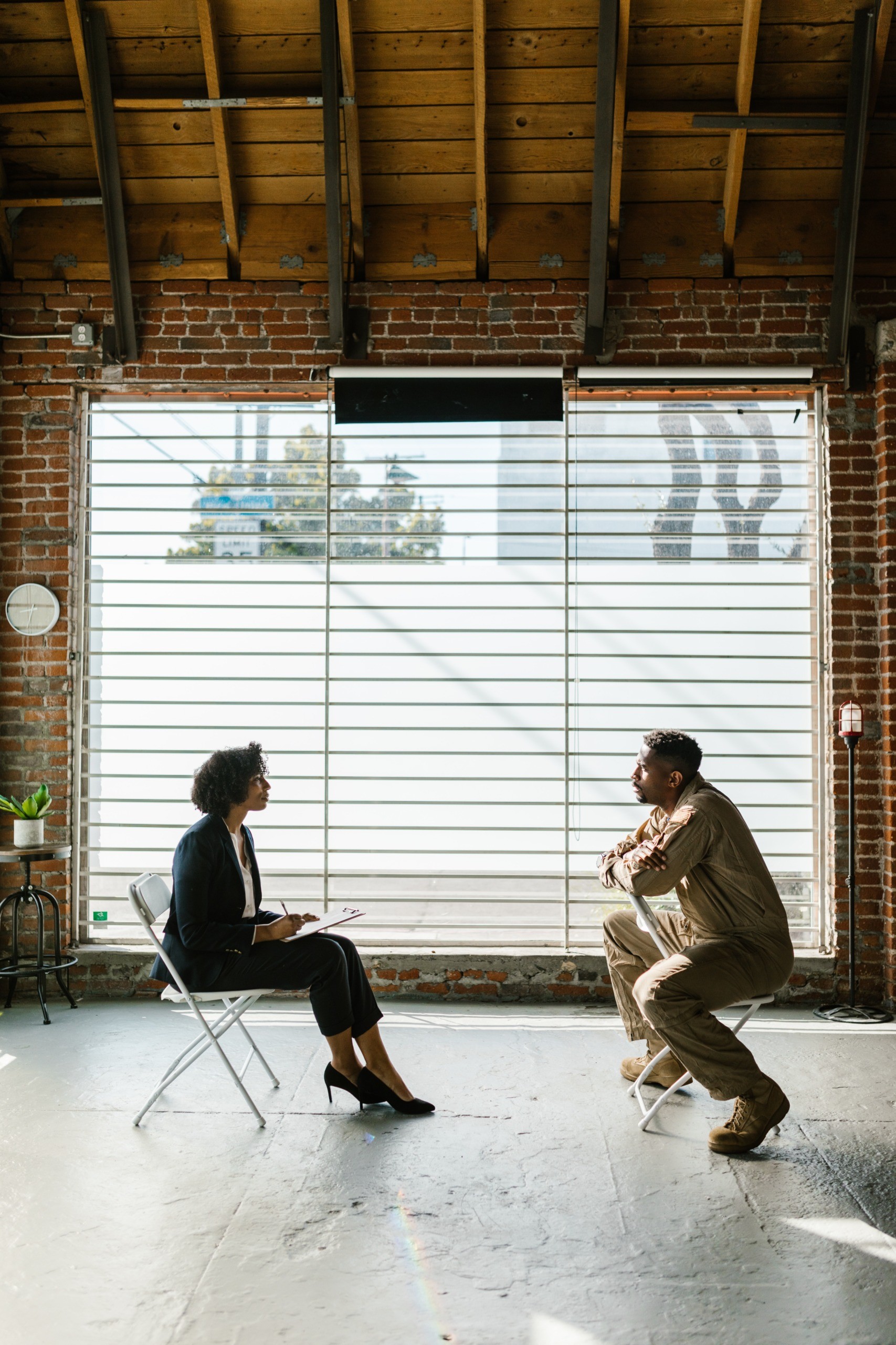 Decorative image of woman and man talking inside in front of a large window, both on chairs. pic by Rodnae Productions courtesy of pexels.