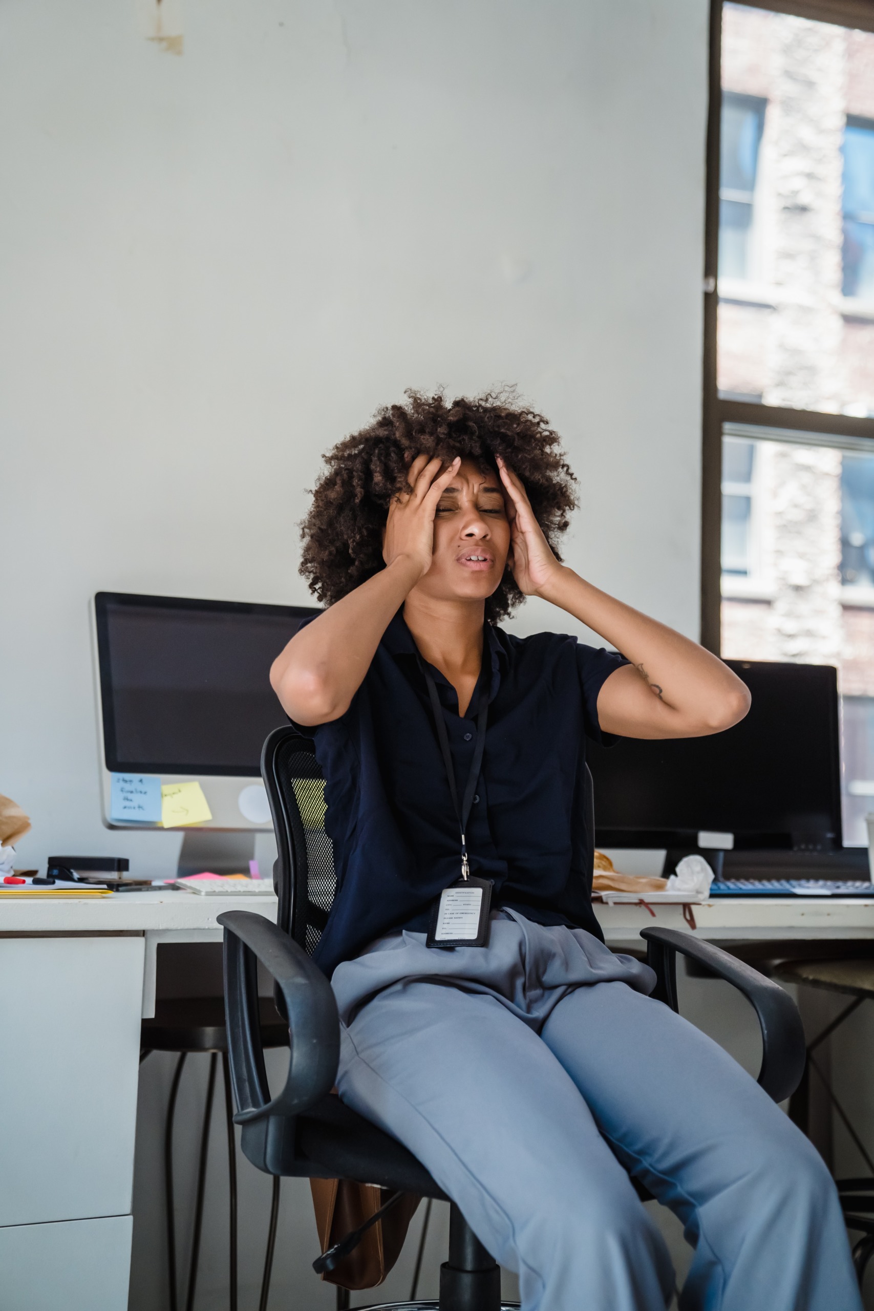 4 Ways to stop anxious thinking image featuring a woman at her desk, clearly anxious, trying to calm herself by rubbing her temples.