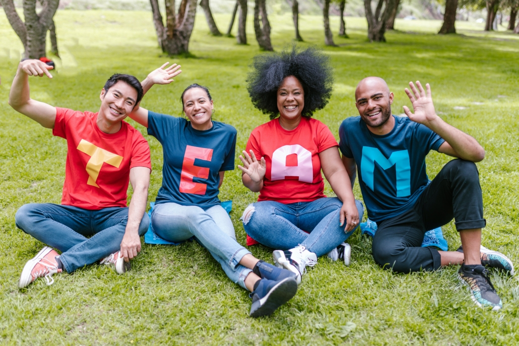 Decorative feature image for blog post 'Unleash Your Facilitation Skills' Discover eight best practices for facilitating effective team meetings. Image features a multicultural team in the park, four members each with a letter on their shirt, spelling out 'TEAM.'