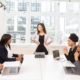 Decorative featured image for Unlock Your Leadership Potential blog post. It features bright conference room with a strong, smiling woman of color leading her team.